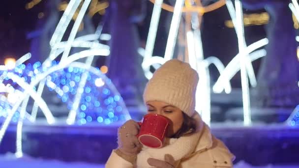 Jeune femme heureuse boit du café ou du vin chaud en plein air en hiver dans les décorations de Noël — Video