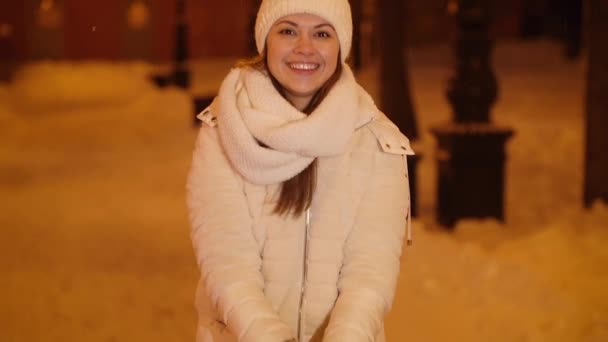 Młoda szczęśliwa dziewczyna rzuca śniegiem na nocną ulicę miasta — Wideo stockowe