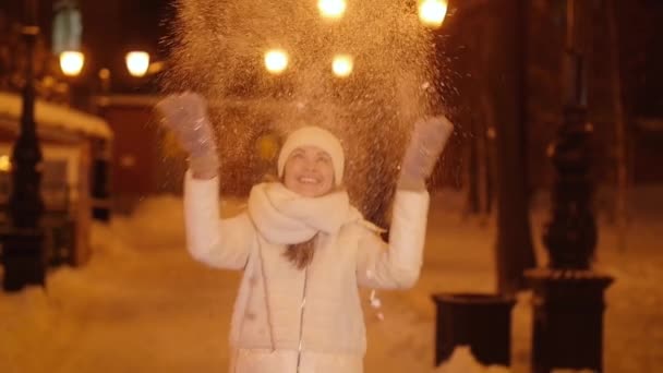 Junges glückliches Mädchen wirft Schnee auf eine nächtliche Straße in der Stadt — Stockvideo