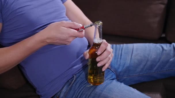 Muž sedící na pohovce otevře láhev piva. — Stock video