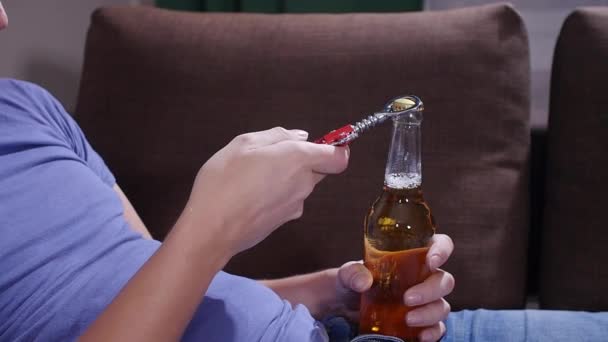 Een man die op een bank zit opent een fles bier. — Stockvideo