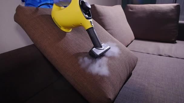 Koncepcja czyszczenia mebli i mieszkań. Mężczyzna sprzątanie kanapy z odkurzaczem parowym w domu — Wideo stockowe