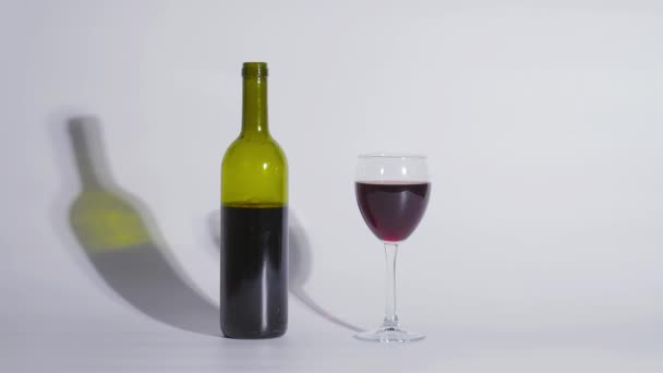 Colpo concettuale, una bottiglia di vino e un bicchiere su sfondo bianco — Video Stock