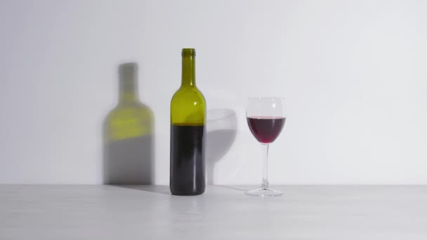 Colpo concettuale, una bottiglia di vino e un bicchiere su sfondo bianco — Video Stock