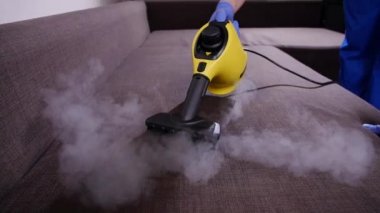 Mobilya ve apartman temizliği konsepti. Kanepeyi buharlı temizleme makinesiyle temizleyen adam.