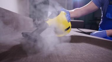 Mobilya ve apartman temizliği konsepti. Kanepeyi buharlı temizleme makinesiyle temizleyen adam.
