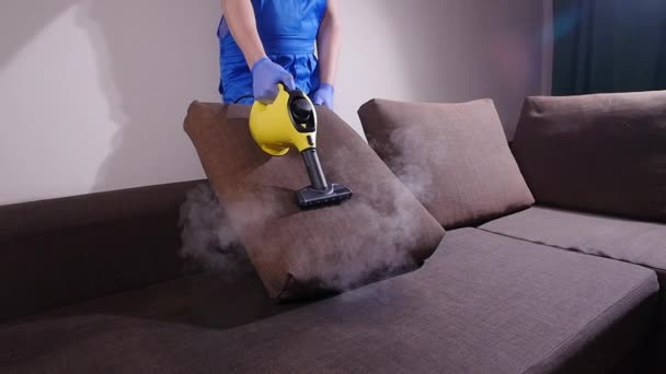 Концепция уборки фасадов и квартир. Мужчина чистит диван с пароочистителем дома — стоковое видео