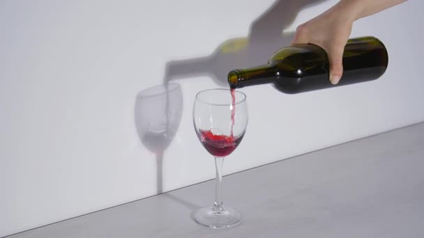 Conceptuele shot, gieten van rode wijn in een glas op een grijze achtergrond — Stockvideo