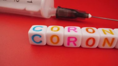 Covid-19 konsepti. Kırmızı zemin üzerinde şırınga bulunan Coronavirus harfleri