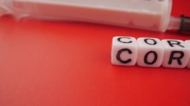 Covid-19 konsepti. Kırmızı zemin üzerinde şırınga bulunan Coronavirus harfleri