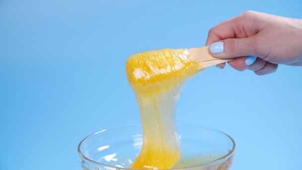 Bellezza e cura del corpo concetto. Pasta o cera di zucchero giallo liquido per depilazione su fondo blu — Video Stock