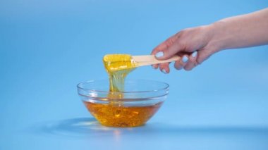 Güzellik ve vücut bakımı kavramı. Mavi arkaplandaki tüy dökümü için sıvı sarı şeker yapıştırıcısı veya ağda