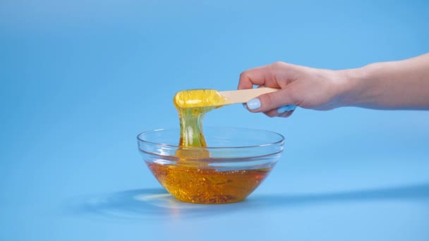Beauty and body care concept. Liquid yellow sugar paste or wax for depilation on a blue background — Stock Video