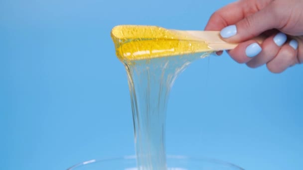 Concept beauté et soin du corps. Pâte à sucre jaune liquide ou cire pour épilation sur fond bleu — Video