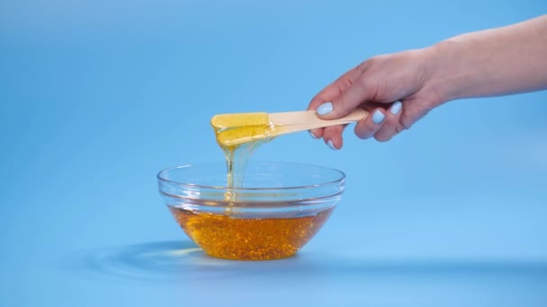 Concepto de belleza y cuidado corporal. Pasta de azúcar amarillo líquido o cera para depilación sobre fondo azul — Vídeos de Stock