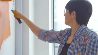 Düz yenileme konsepti. Orta yaşlı mutlu bir kadın boya silindirli, turuncu boyalı beyaz duvar boyuyor.