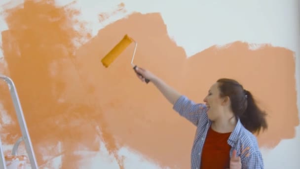 Concepto de estilo de vida singular. Joven mujer feliz pinta sus paredes de naranja con un rodillo — Vídeos de Stock