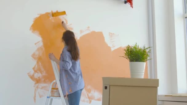 Concetto di stile di vita da single. Giovane donna felice dipinge le sue pareti arancione con un rullo — Video Stock