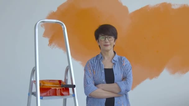 Conceito de renovação plana. Mulher de meia-idade feliz pintando parede branca com rolo de pintura, tinta laranja — Vídeo de Stock