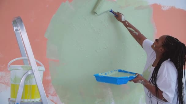 Concepto de renovación plana. Mujer afroamericana sonriente redecorando su casa sosteniendo un rodillo de pintura cubierto de pintura naranja y verde — Vídeo de stock