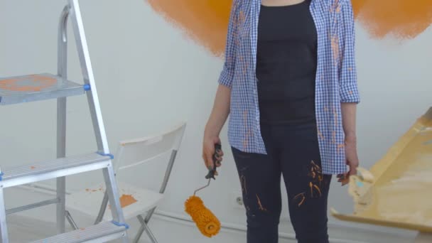 Flat renovation concept. Happy Middle-aged woman painting white wall with paint roller, orange paint — Stock Video