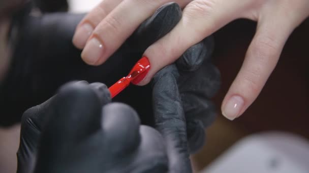 Händerna på en kvinna som applicerar rött nagellack i en skönhetssalong — Stockvideo