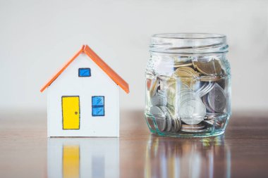 Finans ve bankacılık konsepti için masada ev modeli ile bardakta para.