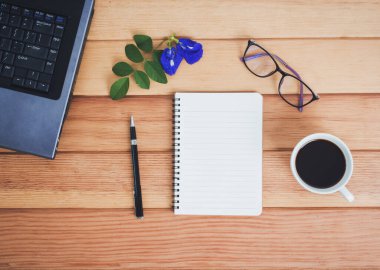 Laptop, akıllı telefon, defter, gözlük, kahve ve kalem ile ofis masasının en üst görüntüsü..