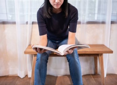 Kafede dergi okuyan Asyalı bir kadın masada oturuyor.