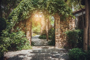 Bahçesinde sarmaşık olan taş kemerli giriş duvarı..