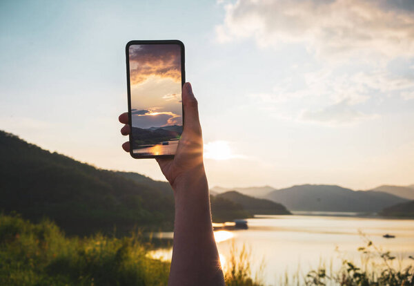 Woman hand using smartphone taking a photo of the sunset with clipping path.