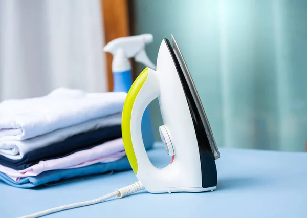 Electric iron and pile of clothes on ironing board