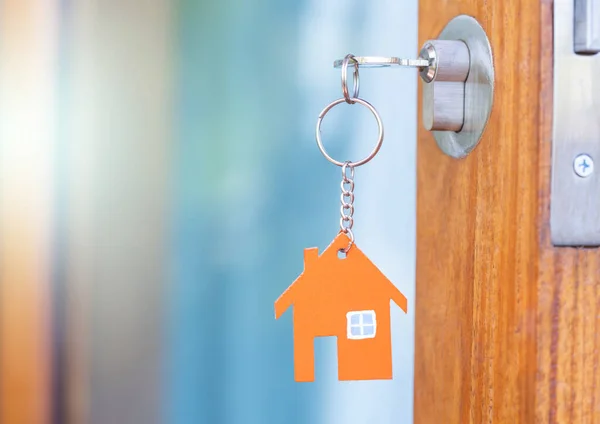 House key in the door with with house shaped keychain.