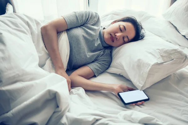 Woman sleeping fell asleep in bed with white screen smartphone. Internet and cell phone addiction.