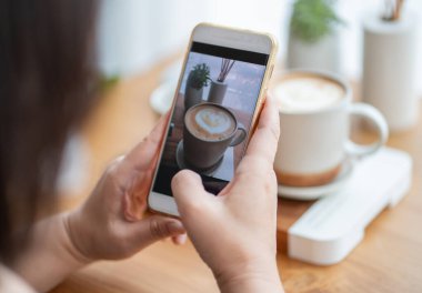 Yakın plan kadın akıllı telefon kullanıyor kahve dükkanındaki masada kahve içiyor.