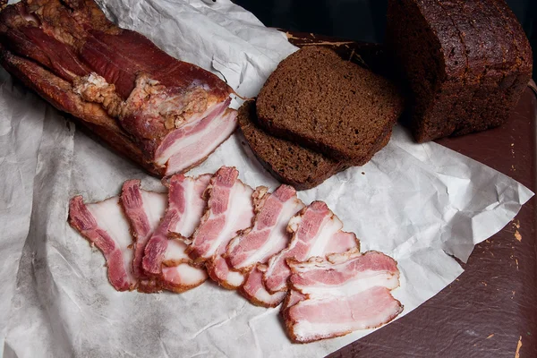 Bladerdeeg gerookt spek met zwarte roggebrood op het papier van verpakking. V — Stockfoto