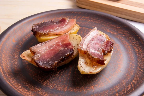 Baked potatoes with slices of bacon on wooden background.