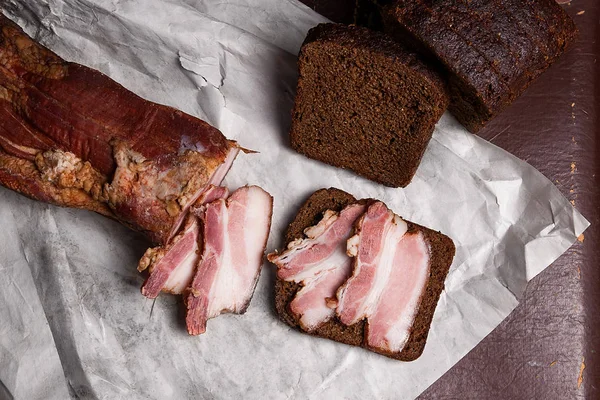 Bladerdeeg gerookt spek met zwarte roggebrood op het papier van verpakking. V — Stockfoto