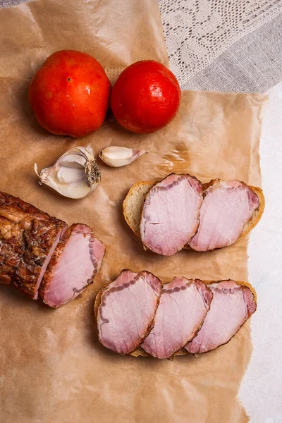 Rebanadas de carne ahumada o jamón sobre papel de embalaje marrón. Tomates, garl —  Fotos de Stock