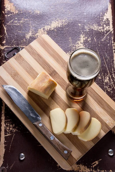 Glass with dark beer with smoked cheese on cutting board. — Stock Photo, Image