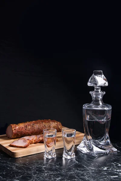 Bouteille et verres à feu avec vodka avec des tranches de viande fumée sur — Photo