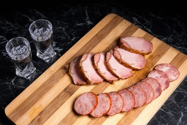 Szklanki z wódki, plasterki wędzonego mięsa i wędliny sausag — Zdjęcie stockowe