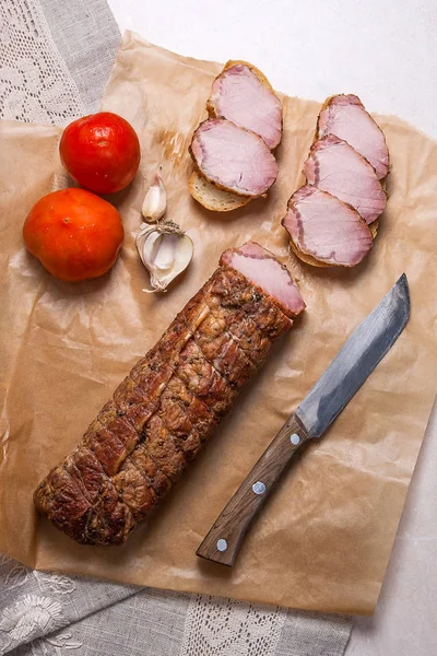 Slices smoked meat or ham and knife on brown packing paper. Toma