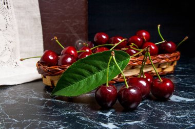 Birkaç kırmızı tatlı kiraz ve büyük yeşil yaprak masanın üzerinde. Nitelikleri