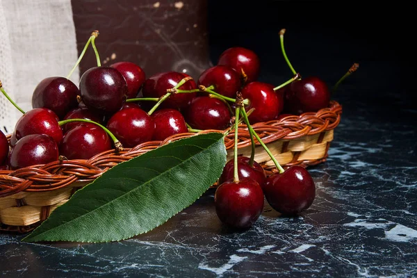 Several red sweet cherries and big green leaf on the table. Fres