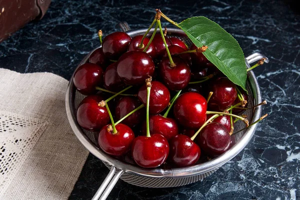 Fresh organic sweet cherry and big green leaf in steel colander