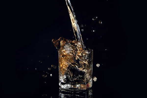 Whiskey pouring into glass with ice isolated on black background — Stock Photo, Image