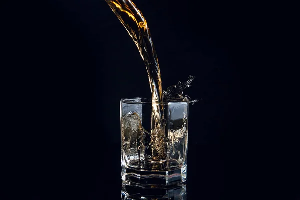 Whiskey pouring into glass with ice isolated on black background — Stock Photo, Image