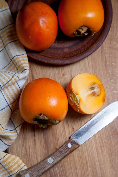 Whole ripe persimmon and sliced fruit on a wooden background — Stock Photo, Image