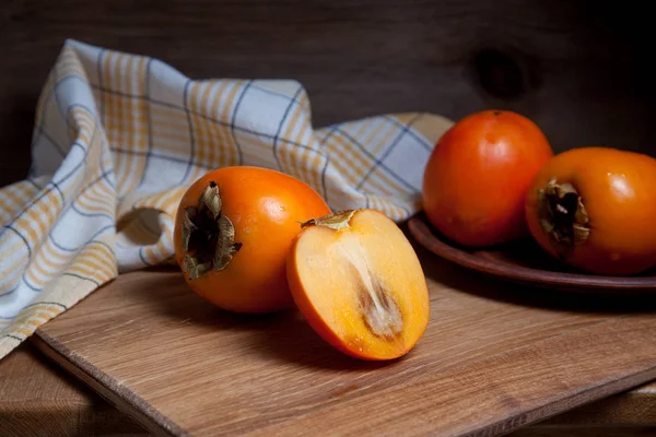 Whole ripe persimmon and sliced fruit on a wooden background — Stock Photo, Image